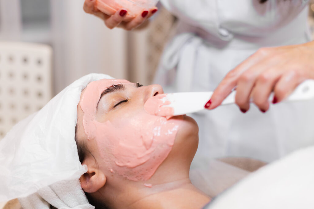 cosmetologist applies alginate mask with spatula on face of woman. facial skin and anti aging treatment. cosmetology and professional facial skin care.