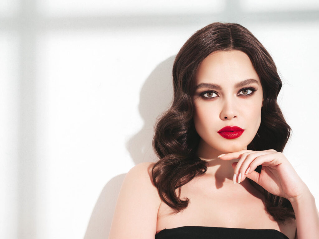beauty portrait of young brunette woman with evening makeup and perfect clean skin. sexy model with curly hair posing in studio. with red bright natural lips